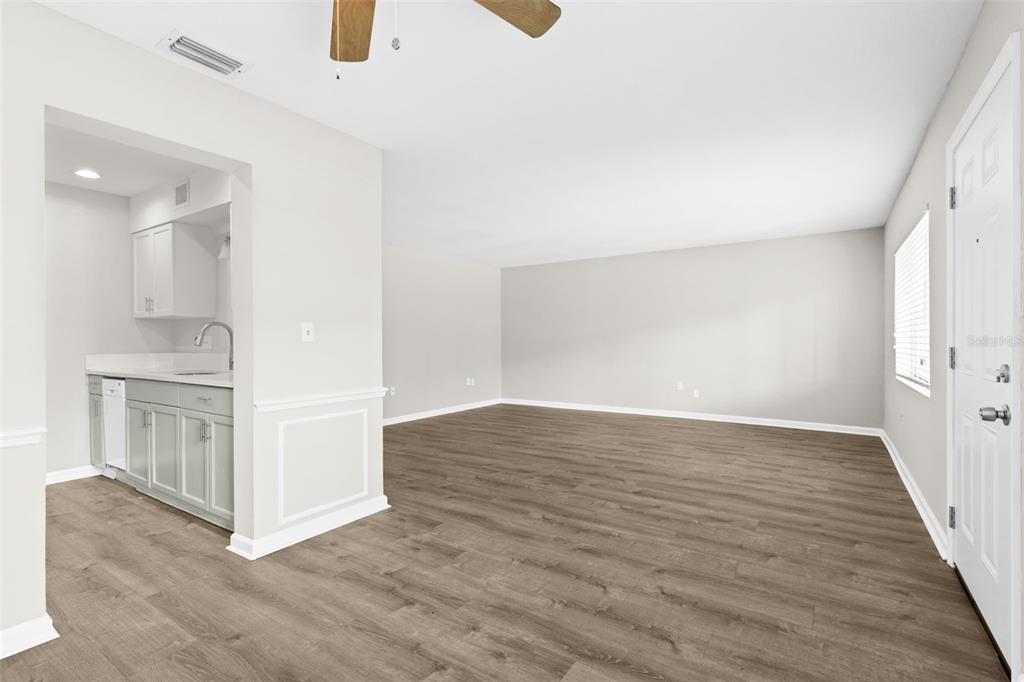 An empty room with light wood-look flooring, white walls, and a small adjacent kitchen area — 350 79TH AVENUE N UNIT 134, ST PETERSBURG, FL