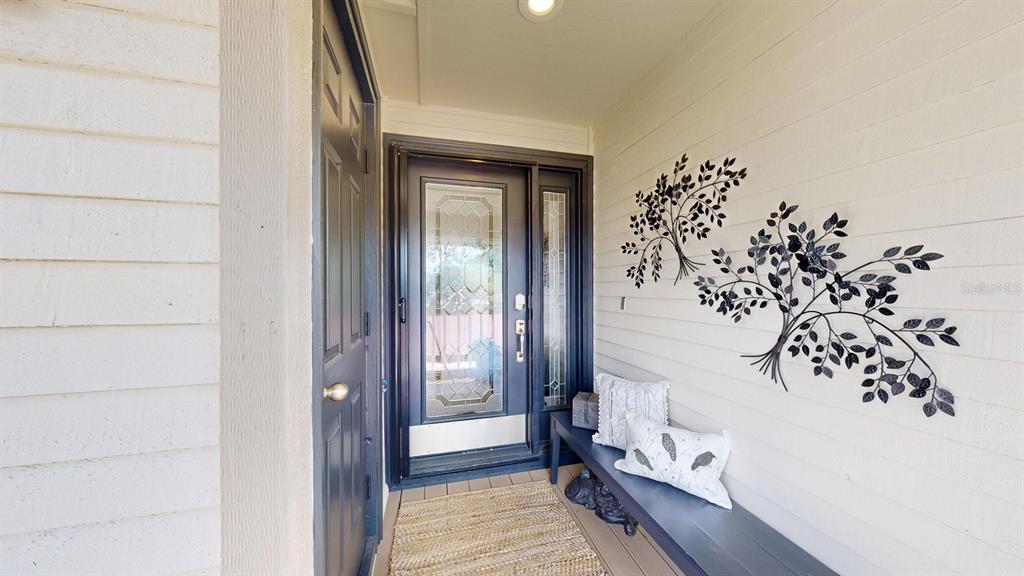 A covered entryway features a dark door, a bench with pillows, and metal tree wall decor — 40 MAGNOLIA DRIVE S. UNIT 0, ORMOND BEACH, FL
