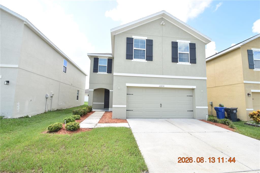 A two-story suburban house features a light-colored stucco exterior, a two-car garage, and dark shutters — 10233 MANGROVE WELL ROAD, SUN CITY CENTER, FL