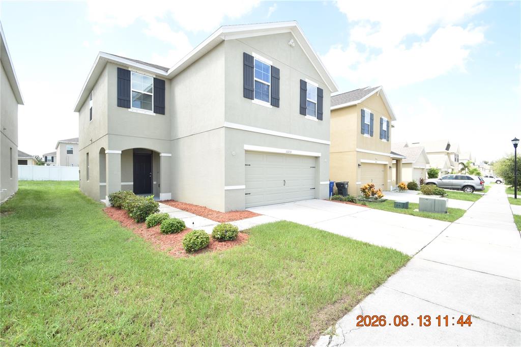 A two-story suburban house with a beige stucco exterior, a garage, and a front lawn — 10233 MANGROVE WELL ROAD, SUN CITY CENTER, FL