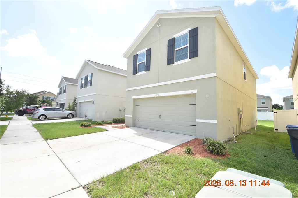 A two-story suburban house features a beige stucco exterior, a two-car garage, and dark shutters — 10233 MANGROVE WELL ROAD, SUN CITY CENTER, FL