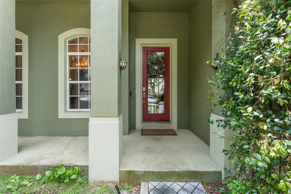 A covered entryway features a red front door, a tall arched window, and green stucco walls — 428 SHADY PINE COURT, MINNEOLA, FL