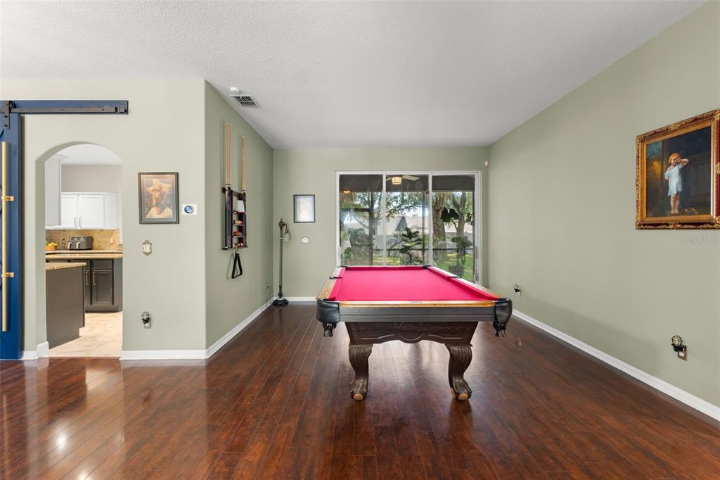 A room with hardwood floors features a red pool table and a view of the outdoors — 428 SHADY PINE COURT, MINNEOLA, FL