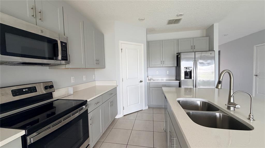 A kitchen features light gray cabinets, stainless steel appliances, a center island, and tile flooring — 486 PINE TREE BRIDGE TRAIL, ST CLOUD, FL