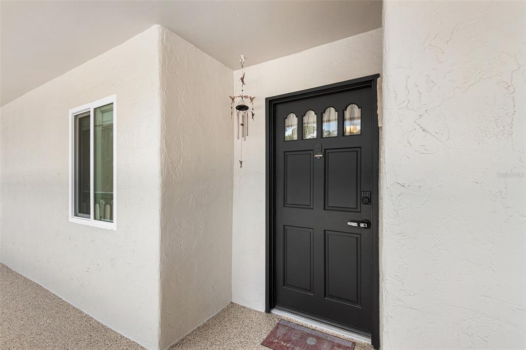 A black front door with glass panels sits on a porch with textured white walls — 1776 6TH STREET NW UNIT 308, WINTER HAVEN, FL