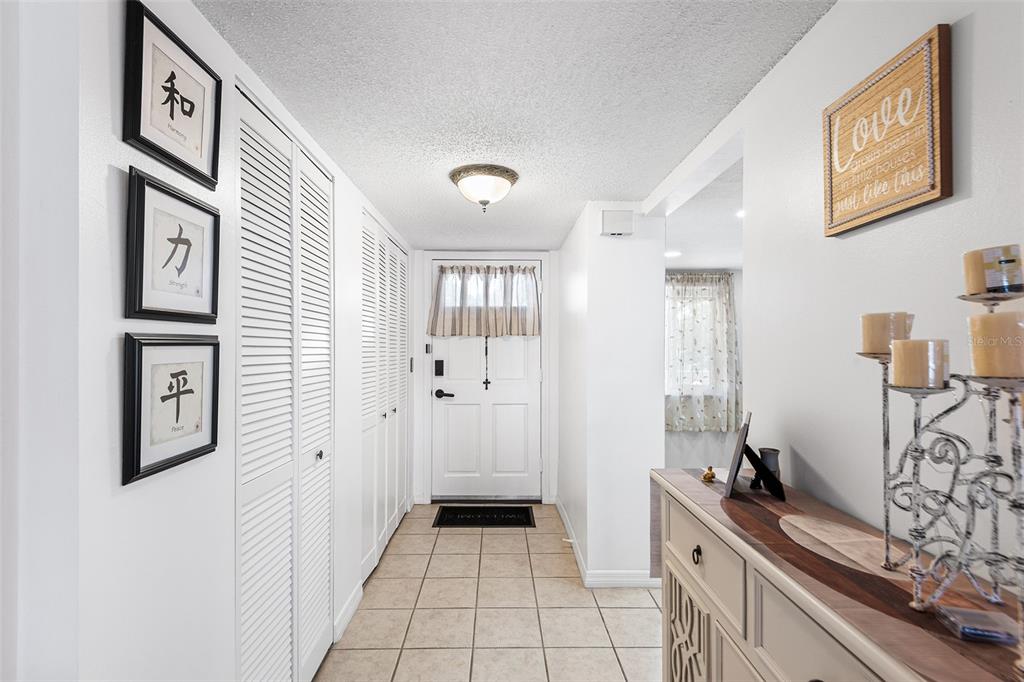 A tiled entryway features white louvered closet doors, wall art, and a wooden console table — 1776 6TH STREET NW UNIT 308, WINTER HAVEN, FL