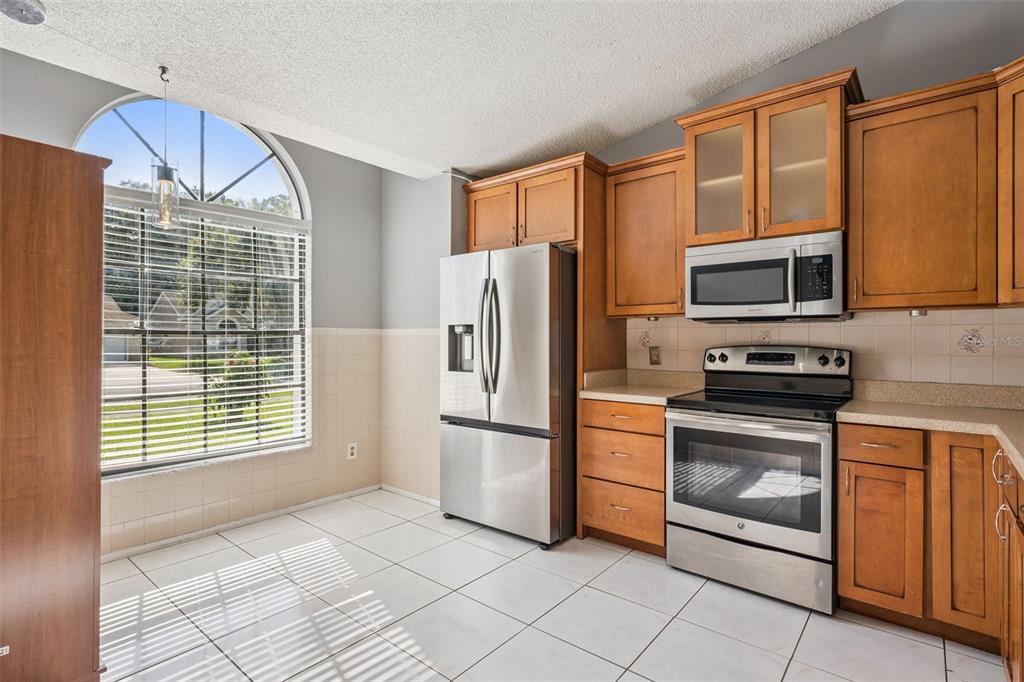 A kitchen features wood cabinets, stainless steel appliances, white tile flooring, and a large arched window — 2136 OPAL DRIVE, ORLANDO, FL