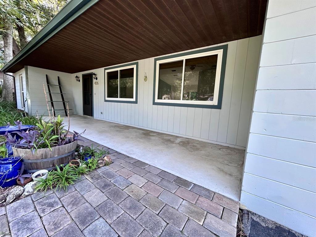 A covered concrete porch features a brick paver walkway and light-colored vertical siding — 4135 NW 30TH TERRACE, GAINESVILLE, FL