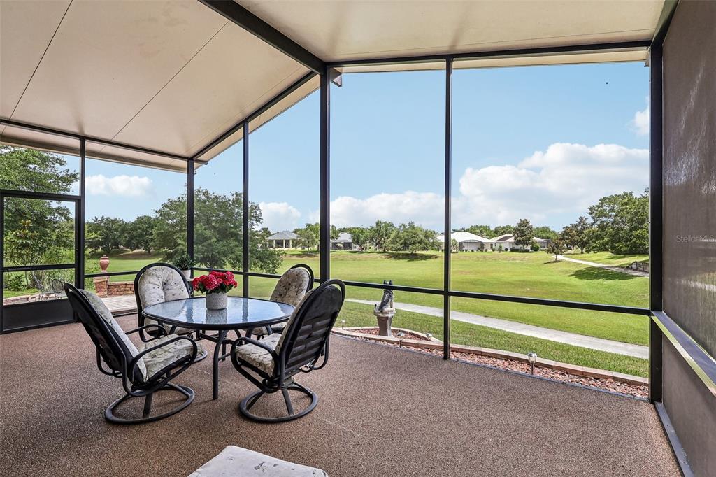 A screened-in patio features a dining set overlooking a grassy golf course landscape — 3538 MULBERRY GROVE LOOP, LEESBURG, FL