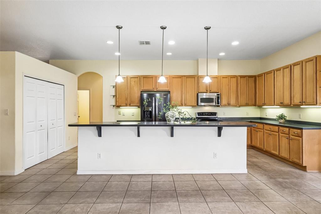 A kitchen features light wood cabinets, a dark countertop island, and tile flooring — 3538 MULBERRY GROVE LOOP, LEESBURG, FL