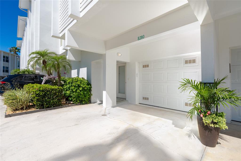 A white garage door is set under a covered entryway with a potted plant nearby — 8280 HARBORSIDE CIRCLE, ENGLEWOOD, FL