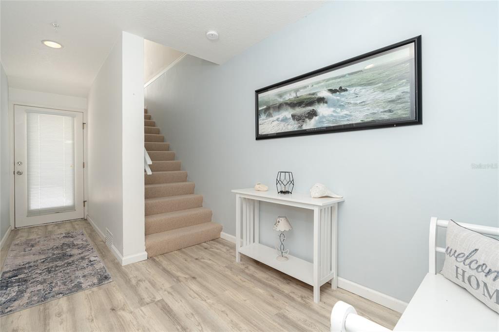 An entryway features light wood flooring, a carpeted staircase, a white console table, and wall art — 8280 HARBORSIDE CIRCLE, ENGLEWOOD, FL