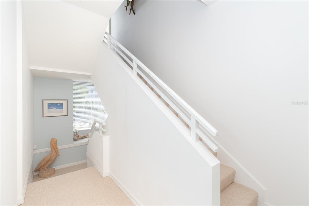 A carpeted staircase with a white railing leads upward past a window and pelican statue — 8280 HARBORSIDE CIRCLE, ENGLEWOOD, FL