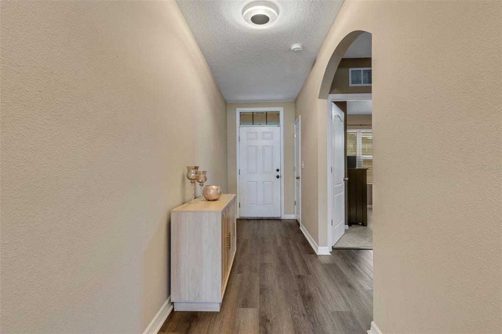 A hallway with wood-look flooring leads to a white front door with a transom window — 15215 PEACEFUL BULL PLACE, BRADENTON, FL