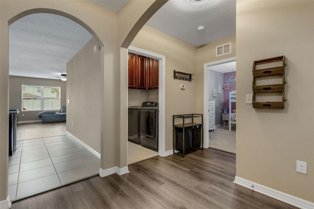 A hallway with wood-look flooring leads to a laundry room and a bedroom — 15215 PEACEFUL BULL PLACE, BRADENTON, FL