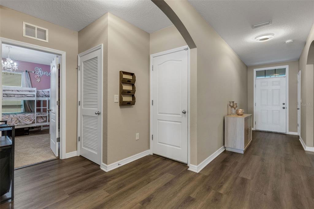 A hallway with wood-look flooring leads to a front door and a bedroom entrance — 15215 PEACEFUL BULL PLACE, BRADENTON, FL