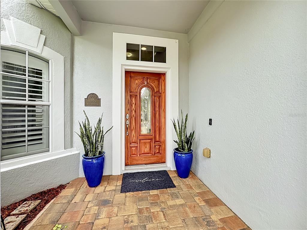 A wooden front door with a glass insert is flanked by two blue potted plants — 2627 LAKEMOOR DRIVE, ORLANDO, FL