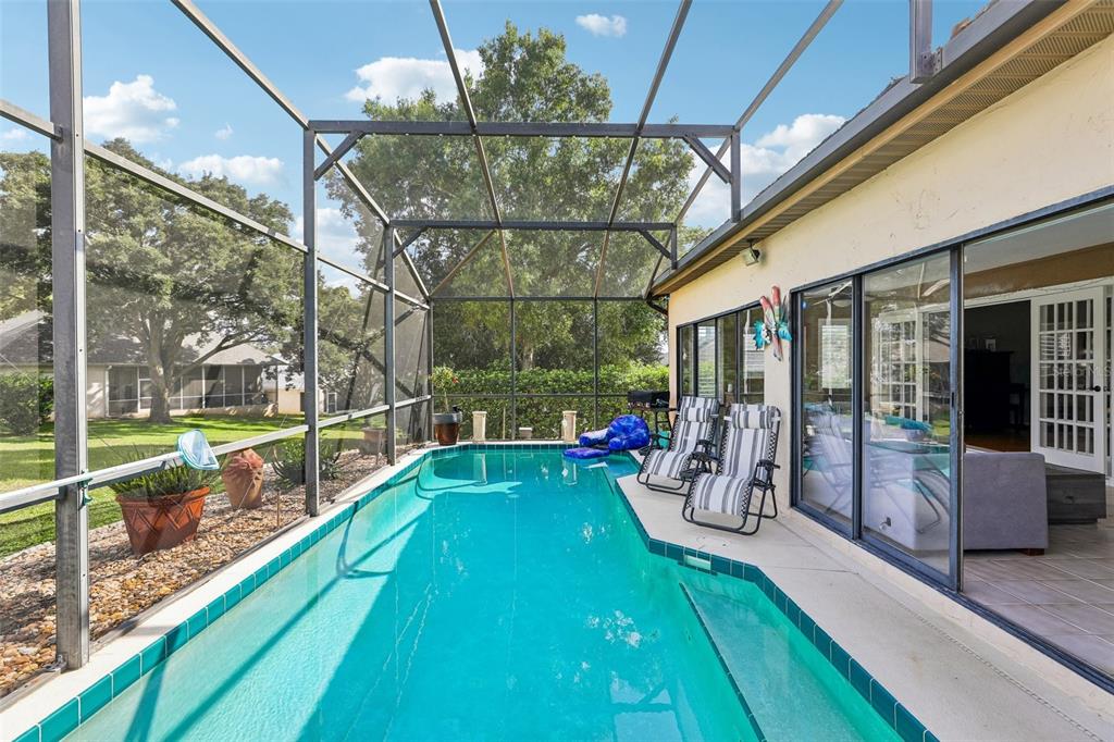 A screened-in swimming pool with patio furniture sits adjacent to a house with sliding doors — 1665 GOLFSIDE VILLAGE BOULEVARD, APOPKA, FL