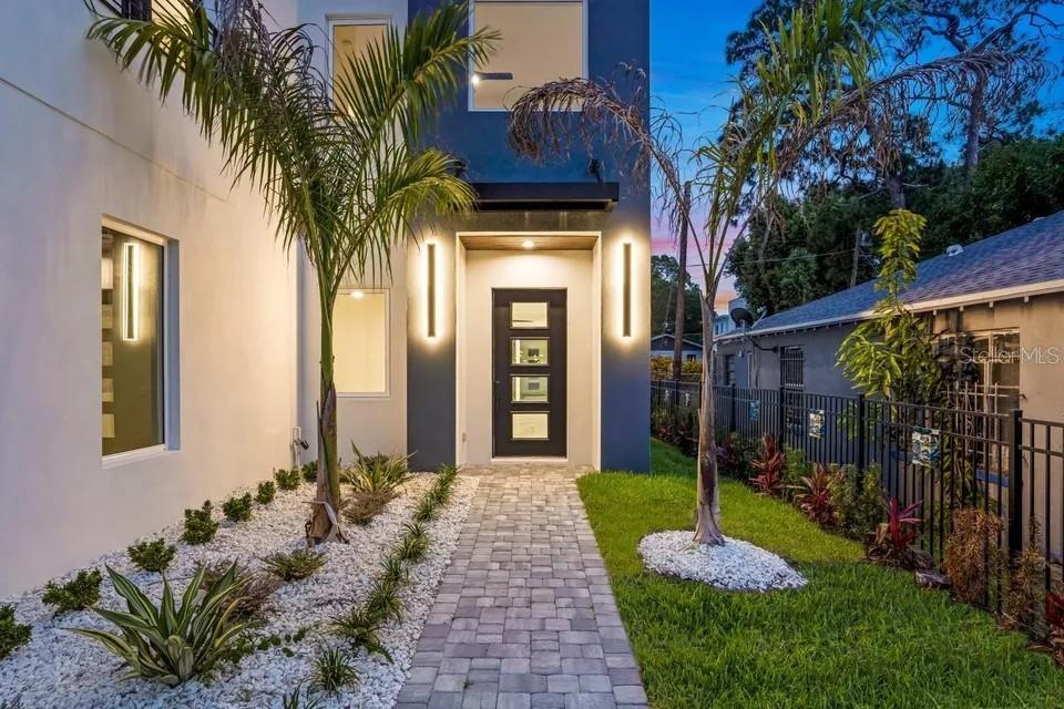 A modern home exterior features a dark gray entrance, a stone walkway, and palm trees — 1156 COCOANUT AVENUE, SARASOTA, FL
