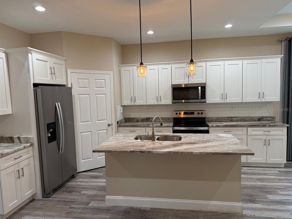A kitchen features white cabinets, a stone-topped island with a sink, and stainless steel appliances — 540 LINDSAY ANNE COURT, PLANT CITY, FL