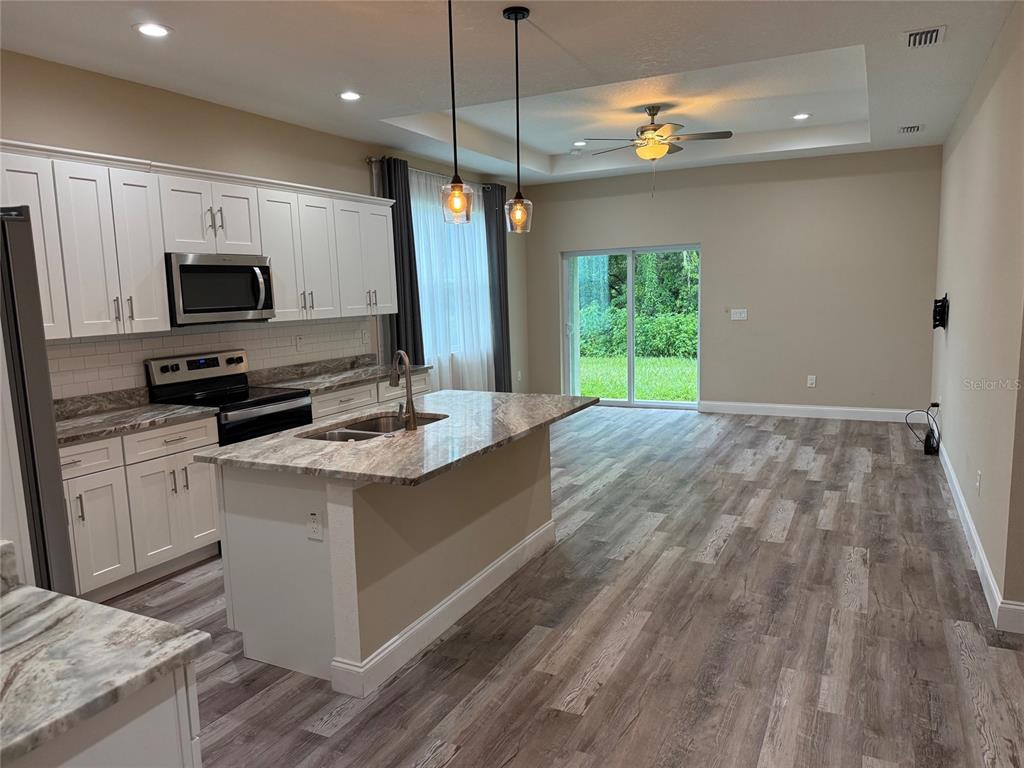 A kitchen with white cabinets, granite countertops, and an island opens to a living area — 540 LINDSAY ANNE COURT, PLANT CITY, FL