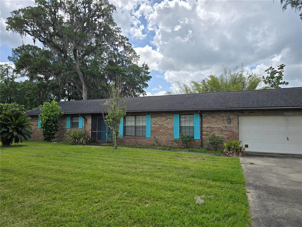 A single-story brick house features a dark shingled roof, blue shutters, and an attached garage — 4506 SE 7TH PLACE, OCALA, FL