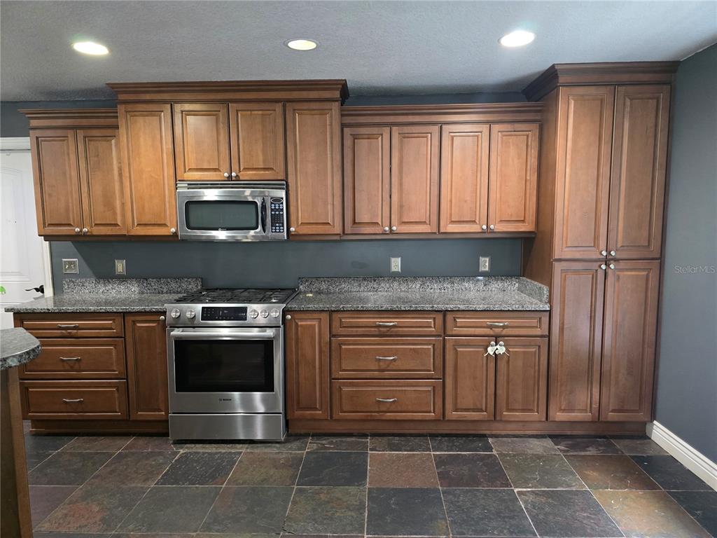 A kitchen features wood cabinets, stainless steel appliances, granite countertops, and dark slate tile flooring — 4506 SE 7TH PLACE, OCALA, FL