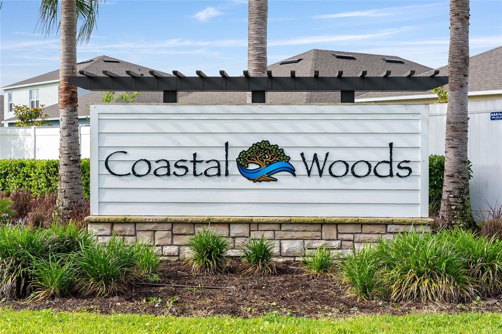 A sign for the Coastal Woods community stands in front of houses and palm trees — 2694 NEVERLAND DRIVE, NEW SMYRNA BEACH, FL