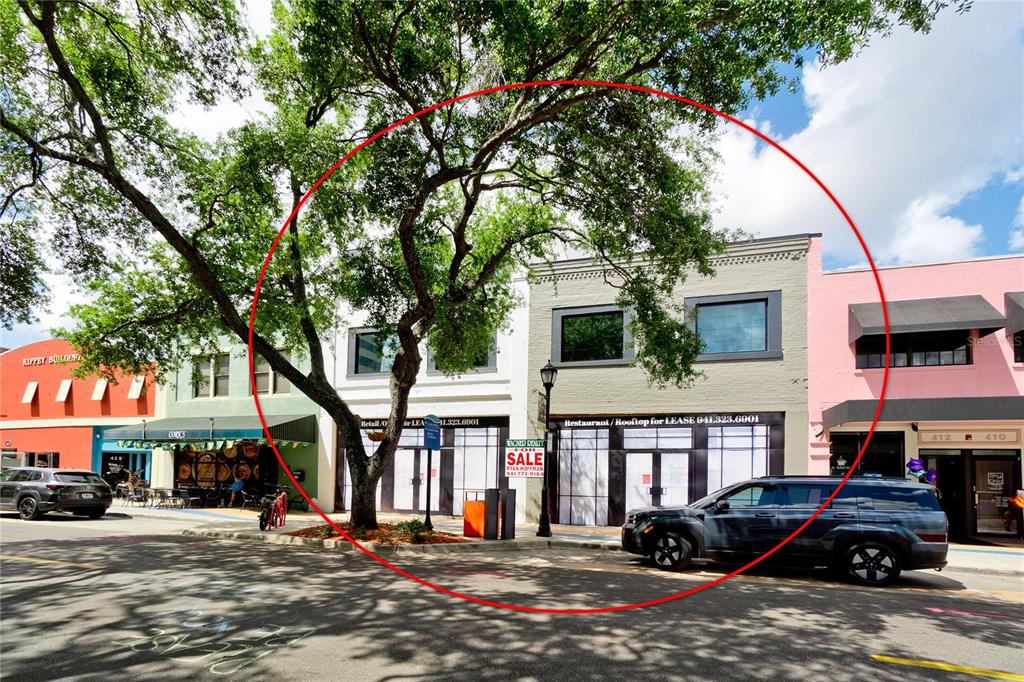 A two-story commercial building with a for sale sign stands on a tree-lined street — 420 12TH STREET W, BRADENTON, FL