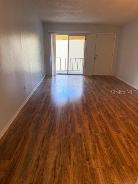 An empty room features wood-look flooring, a sliding glass door to a balcony, and a door — 7523 DOLONITA DRIVE UNIT 7523, TAMPA, FL