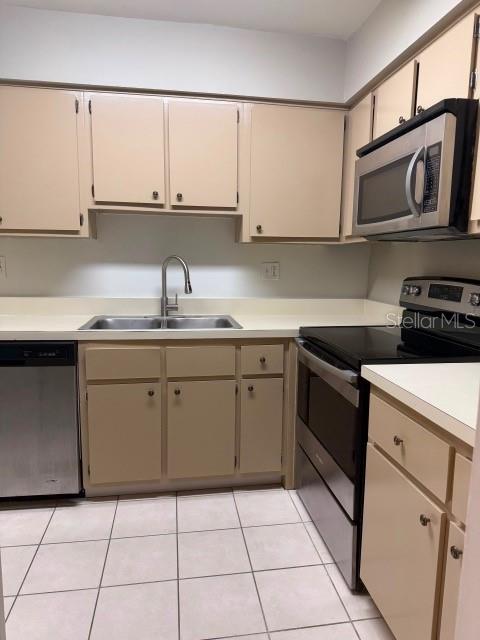 A kitchen features beige cabinets, stainless steel appliances, a double sink, and white tile flooring — 7523 DOLONITA DRIVE UNIT 7523, TAMPA, FL