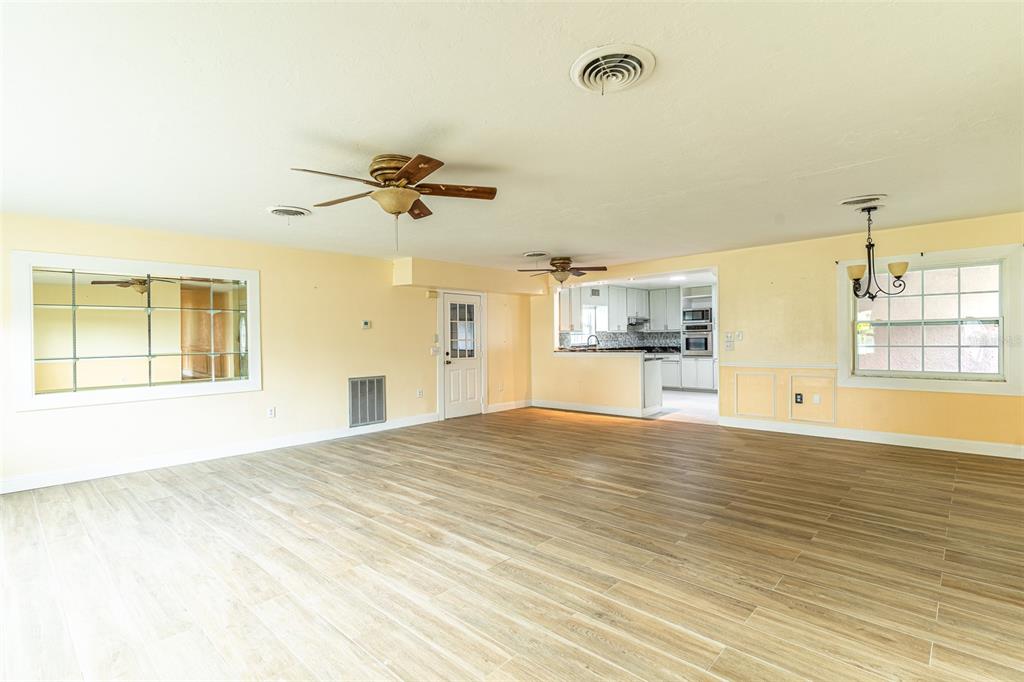 A spacious living area with light wood-look tile flooring, two ceiling fans, and a kitchen pass-through — 3510 LAKEVIEW DRIVE, SEBRING, FL