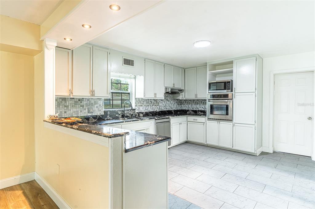 A kitchen with white cabinets, dark granite countertops, a tiled backsplash, and light-colored floor tiles — 3510 LAKEVIEW DRIVE, SEBRING, FL
