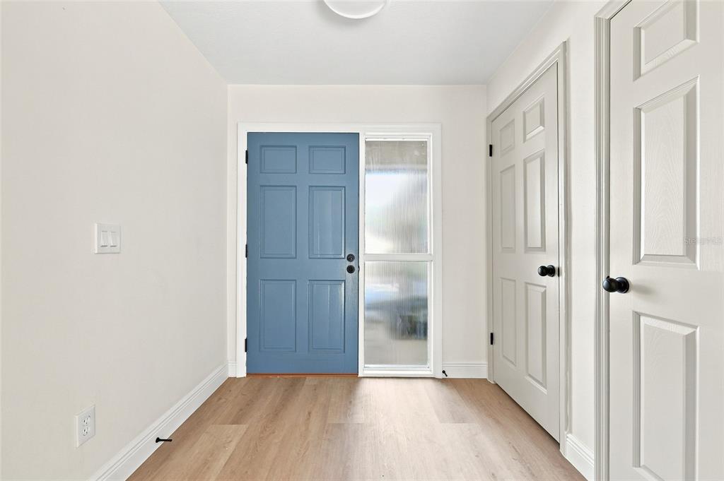 An entryway features a blue front door, light wood-look flooring, and two white closet doors — 1011 MANCHESTER CIRCLE, WINTER PARK, FL