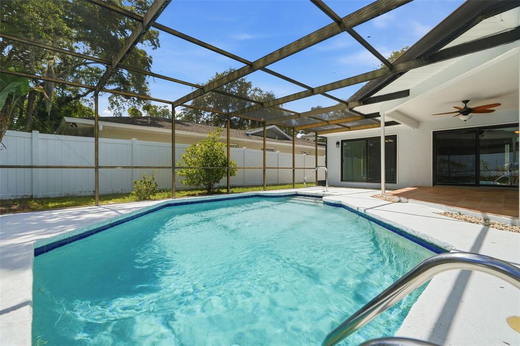 An open-concept living area features wood-look flooring, a stone accent wall, and a pool view — 104 NESTLEBRANCH DRIVE, SAFETY HARBOR, FL