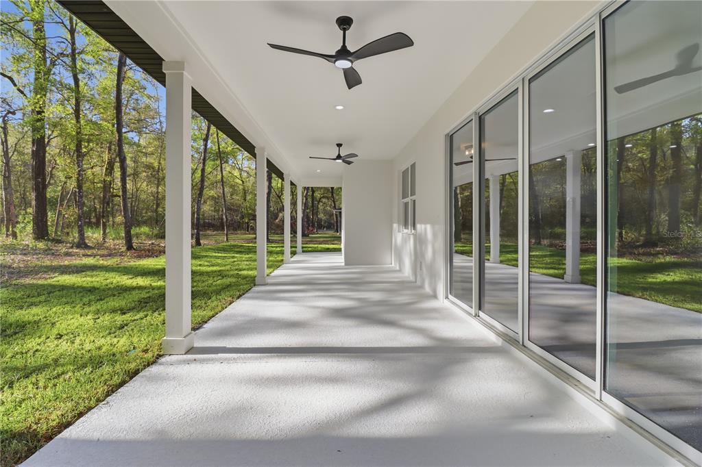A covered concrete patio features white columns, ceiling fans, and large glass sliding doors — 19126 SW 101ST STREET, DUNNELLON, FL