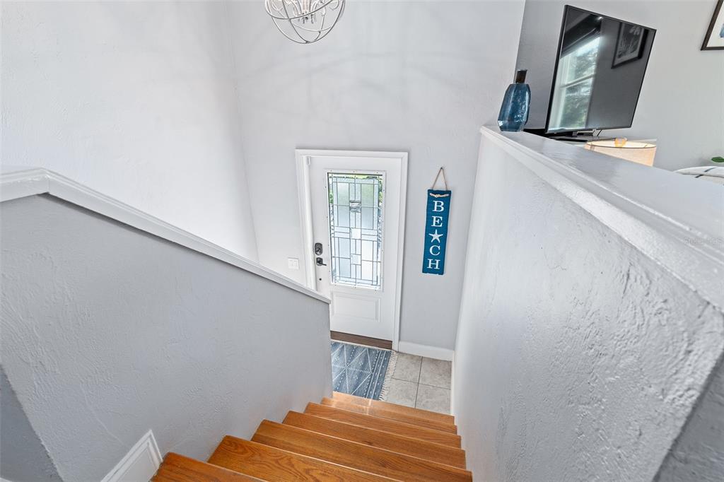 A staircase with wooden treads leads down to a front door with a decorative glass insert — 1843 OAK PLACE, FLAGLER BEACH, FL