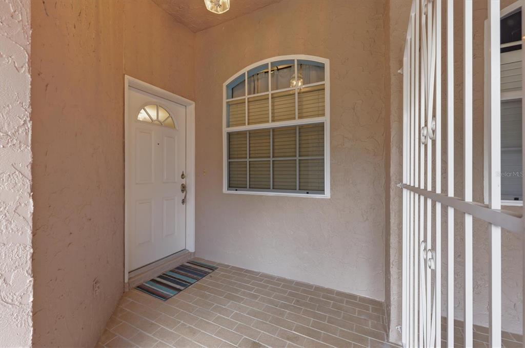 A covered entryway features a white front door, a multi-pane window, and brick flooring — 2175 LYNX RUN, NORTH PORT, FL