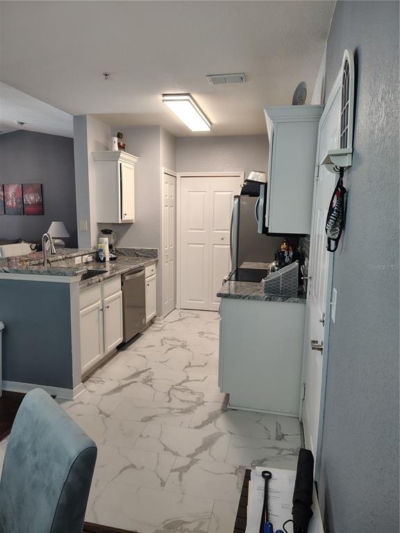 A kitchen features white cabinets, granite countertops, stainless steel appliances, and white marble-patterned tile flooring — 5550 E MICHIGAN STREET UNIT 2328, ORLANDO, FL