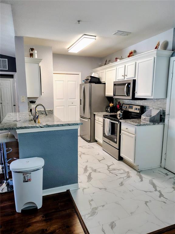 A kitchen features white cabinets, stainless steel appliances, granite countertops, and marble-look tile flooring — 5550 E MICHIGAN STREET UNIT 2328, ORLANDO, FL