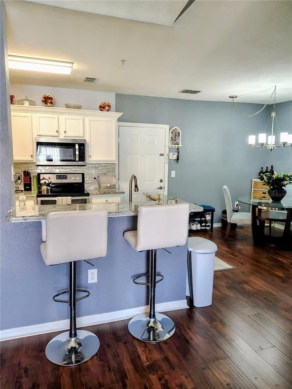 A kitchen with white cabinets, granite countertops, and a breakfast bar with two stools — 5550 E MICHIGAN STREET UNIT 2328, ORLANDO, FL