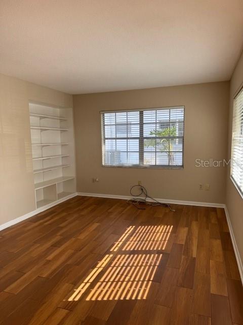 An empty room features wood-look flooring, a built-in bookshelf, and a window with blinds — 225 3RD, MOUNT DORA, FL