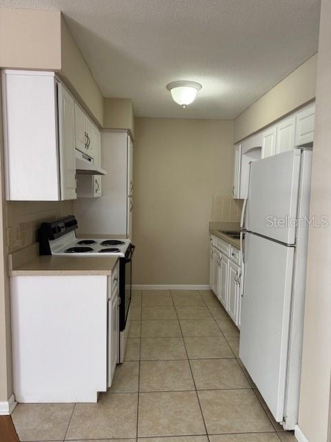 A galley kitchen features white cabinets, a white stove, and a white refrigerator on tile flooring — 225 3RD, MOUNT DORA, FL