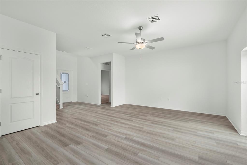 A bright, empty room features light wood-look flooring, white walls, and a ceiling fan — 13348 TULA LOOP, ASTATULA, FL