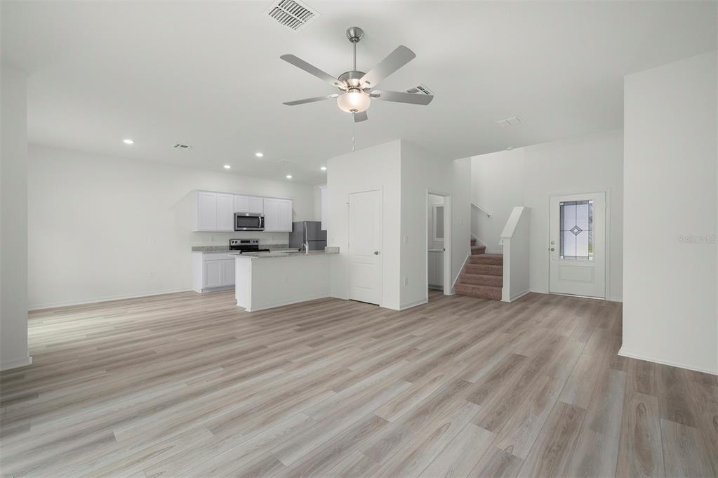 An open-concept living area features light wood-look flooring, a kitchen with white cabinets, and stairs — 13348 TULA LOOP, ASTATULA, FL