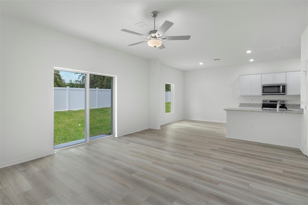 A bright, open-concept living area features light wood-look flooring, a ceiling fan, and sliding doors — 13348 TULA LOOP, ASTATULA, FL