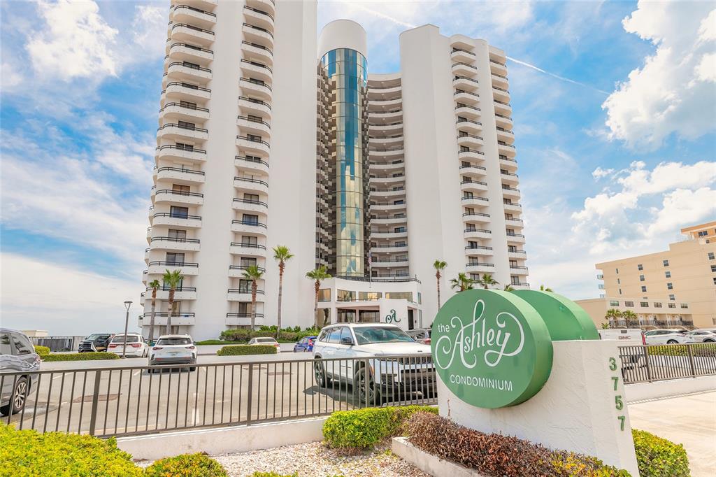 A tall white condominium building stands behind a green sign and a parking lot — 3757 S ATLANTIC AVENUE UNIT 1104, DAYTONA BEACH SHORES, FL