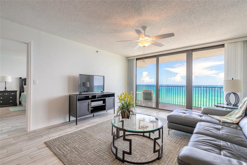A living room with a gray sectional, glass coffee table, and sliding doors overlooking the ocean — 3757 S ATLANTIC AVENUE UNIT 1104, DAYTONA BEACH SHORES, FL