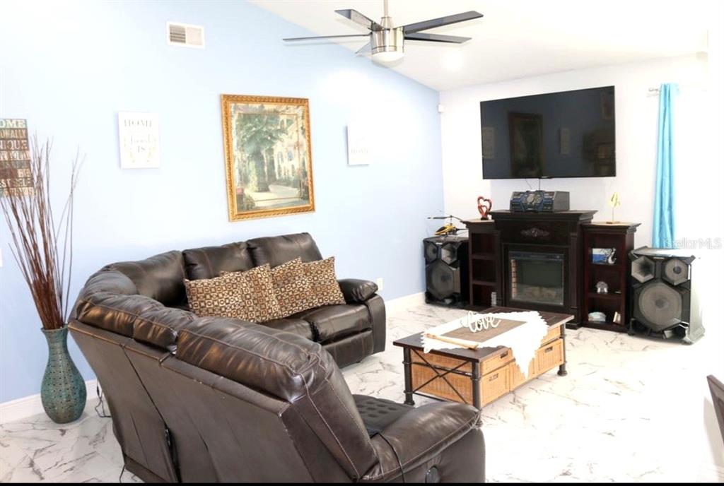 A living room features a dark leather sofa, a fireplace with a television, and tiled floors — 2609 MILL RUN BOULEVARD, KISSIMMEE, FL