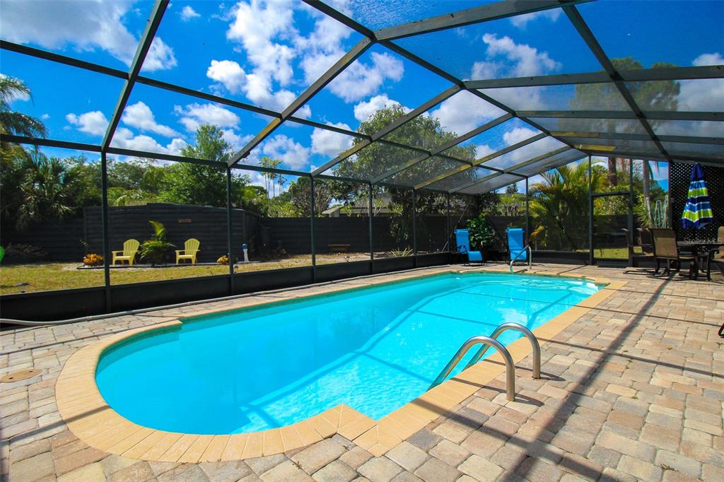 A swimming pool with a screen enclosure sits on a paved patio in a backyard — 3852 GATEWOOD DRIVE, SARASOTA, FL